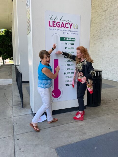 Two volunteers show thermometer banner showing money raised for library renovation campaign