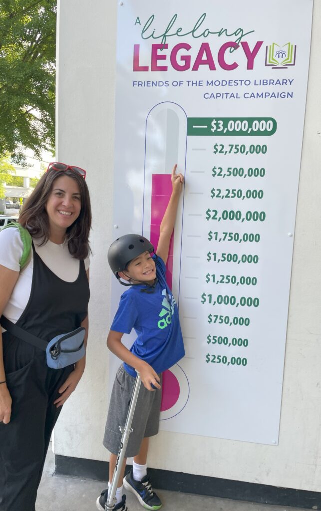 A child stsands with his mother and points to the fundraising thermometer to show how much money has been raised.