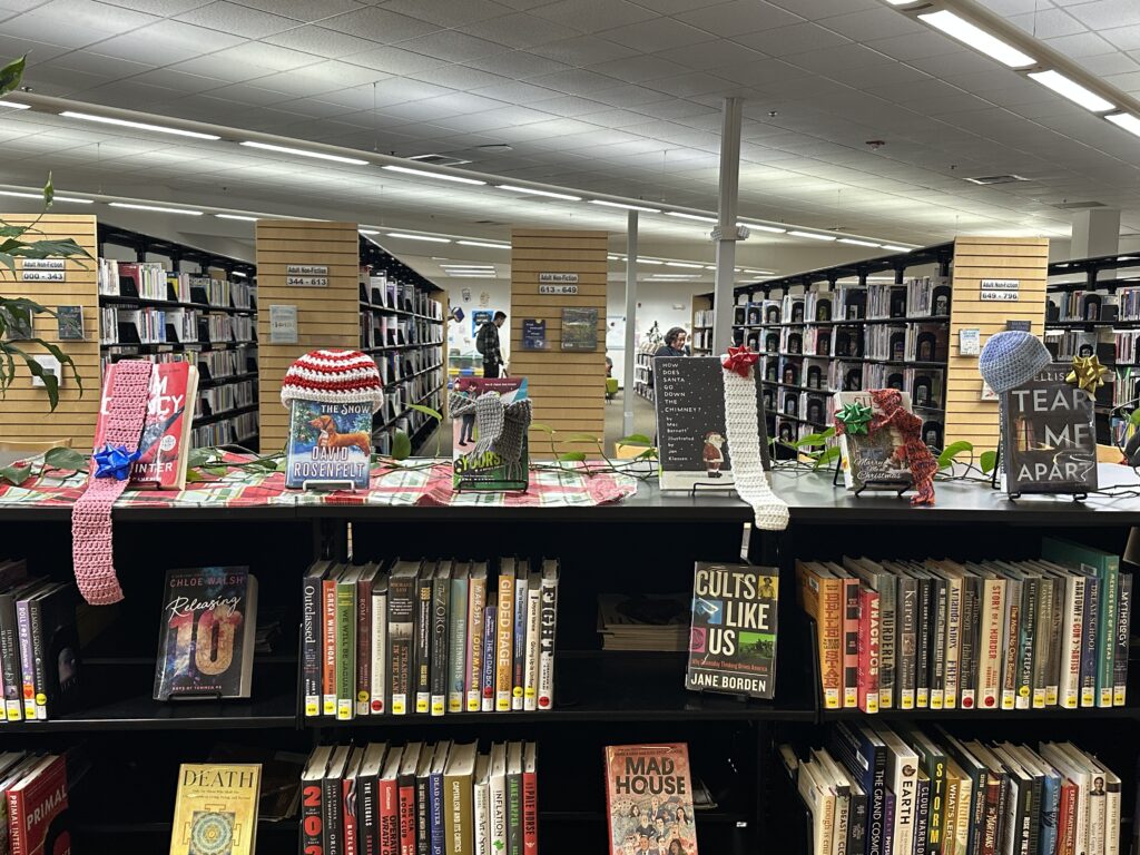 Books displayed on library shelves are adorned with handmade scarves and hats.