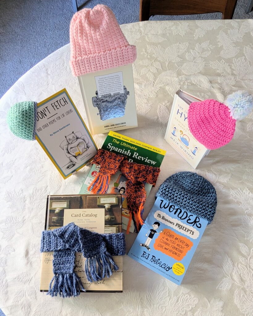 Small yarned hats are propped on displayed books while scarves are wrapped around others.