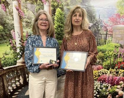 Two women smile as they hold the framed Shining Star Awards they received. 
