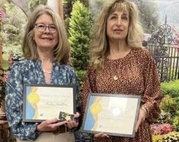 Two women smile as they hold the Shining Star Award plaques they received.